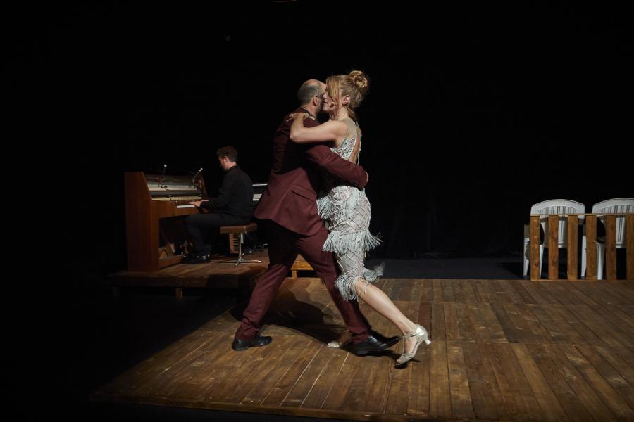 A man and a woman dancing in a semi-dark waltz, on a brown wooden floor